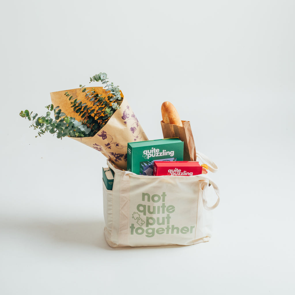 Canvas tote bag with books, puzzles, groceries, flowers, and other items on a light background