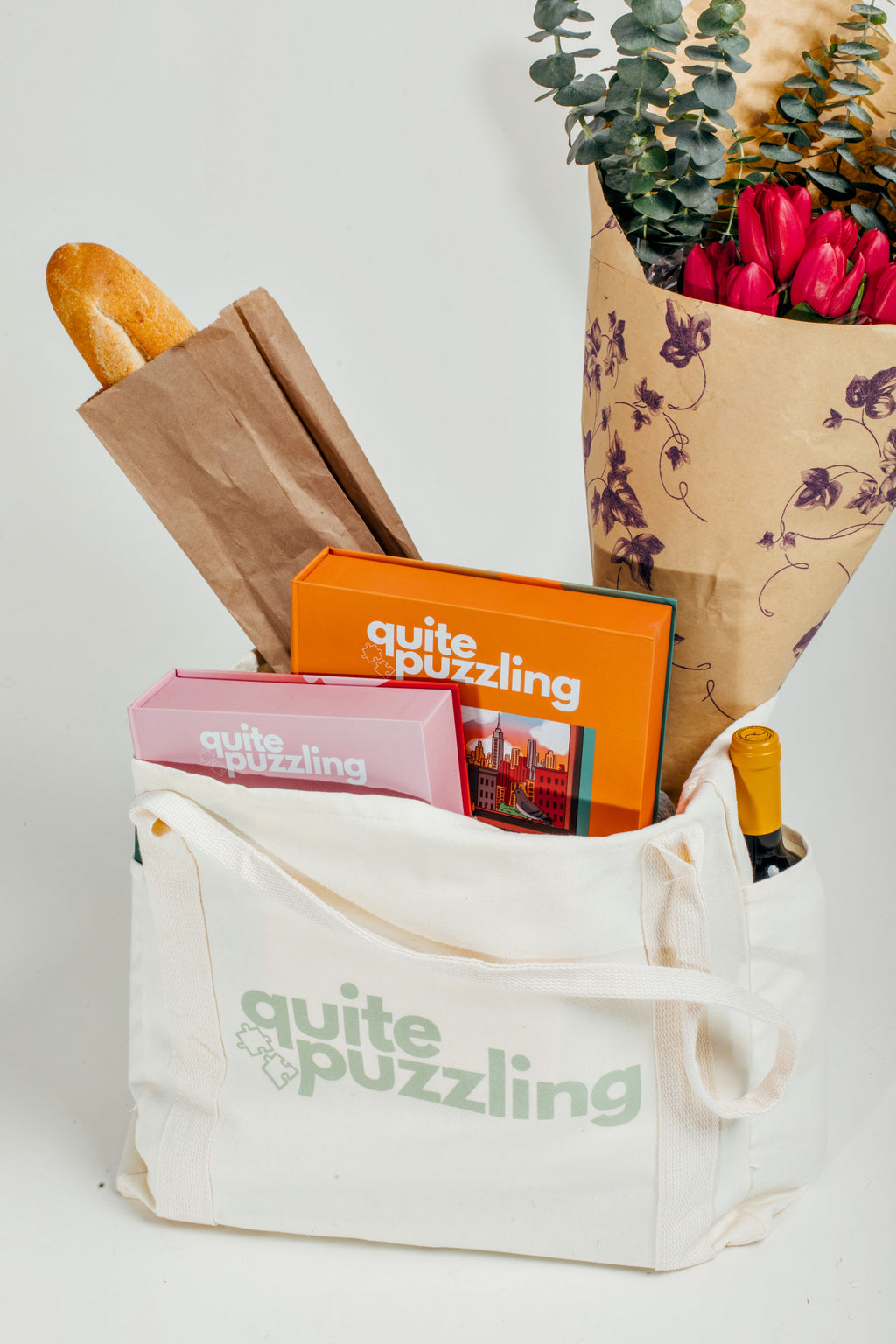White tote bag with 'quite puzzling' branding, containing books, a bouquet of flowers, and bread.